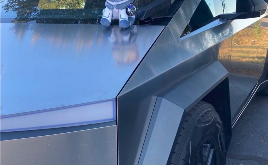 Pelúcia Asteroid Shiba com capacete de astronauta sobre uma Tesla Cybertruck