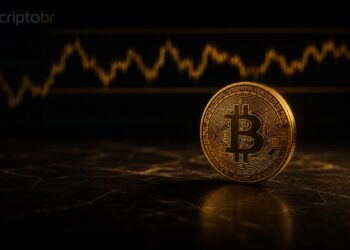 Moeda de Bitcoin em destaque sobre mesa escura com gráfico desfocado ao fundo